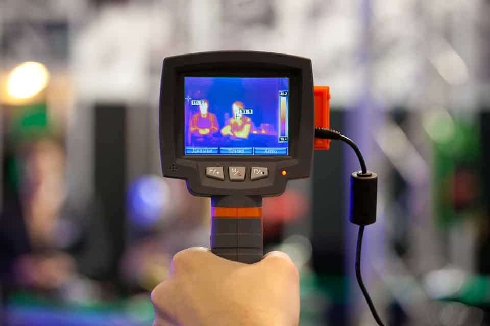 Handheld thermal camera displaying a thermal image of two people, representing a refresher course