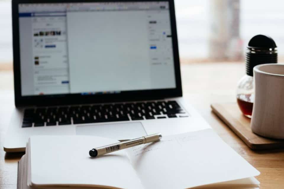 Laptop on a desk with an open notebook and a coffee mug, ready for an online webinar session