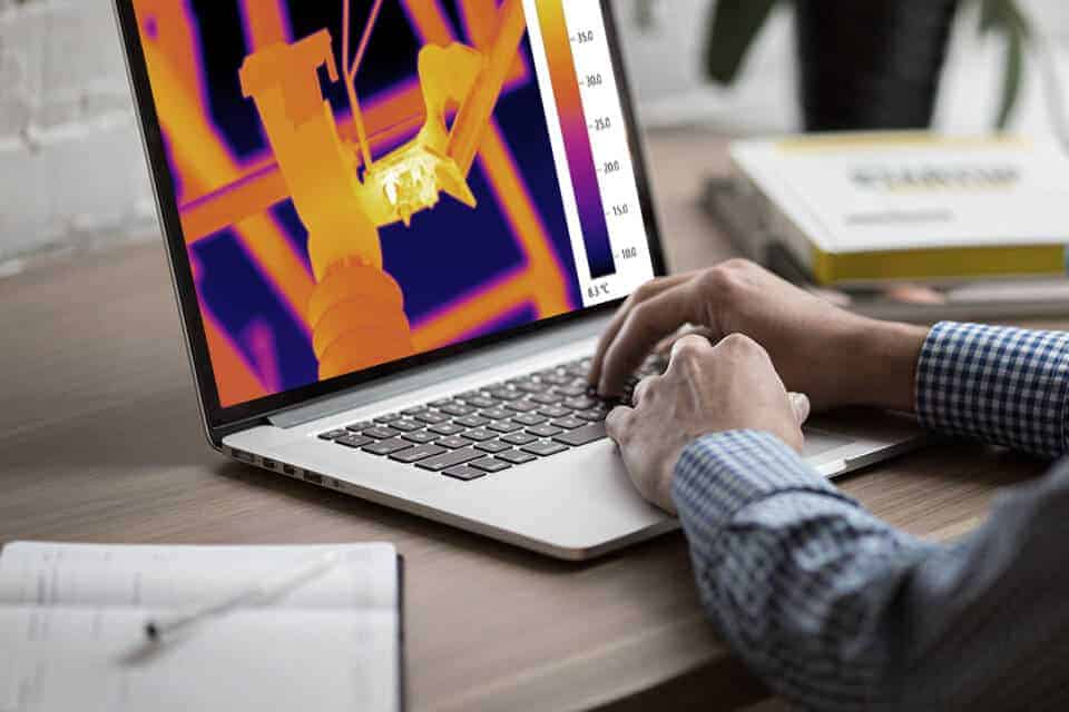 Learner at a laptop reviewing a thermal image of electrical equipment, representing distance learning